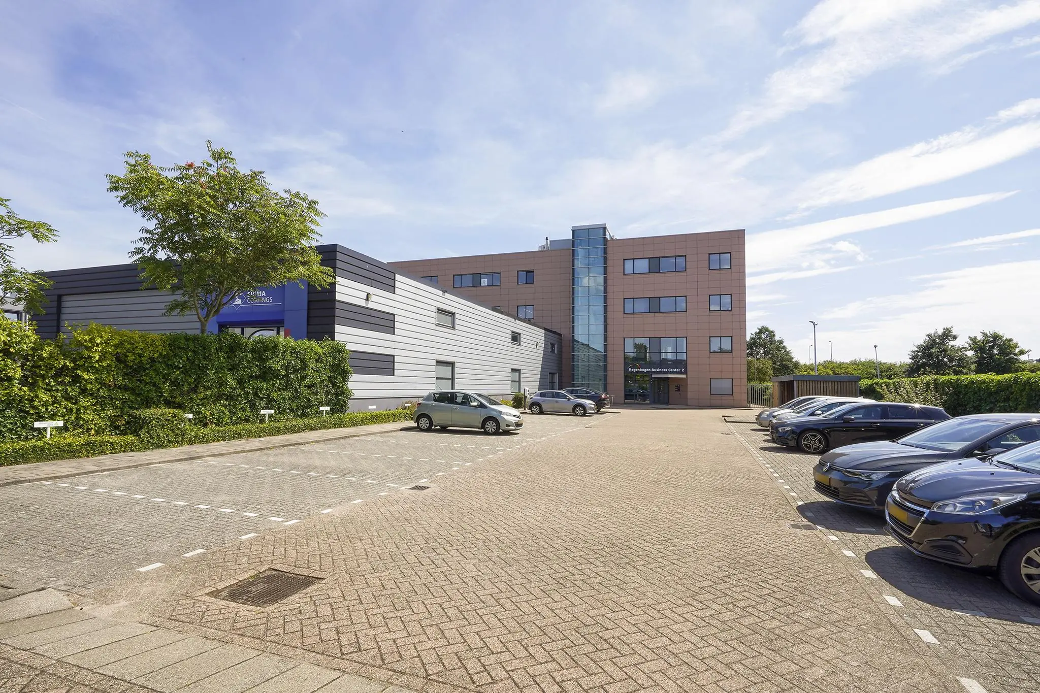 Kantoorgebouw aan de Laan van 's-Gravenmade met parkeerplaatsen op de voorgrond op een zonnige dag.